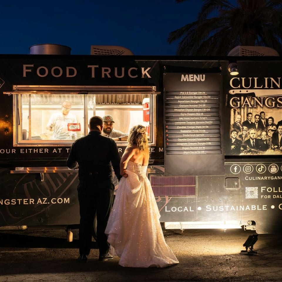 A couple in formal wear orders from the illuminated Culinary Gangster food truck at night.