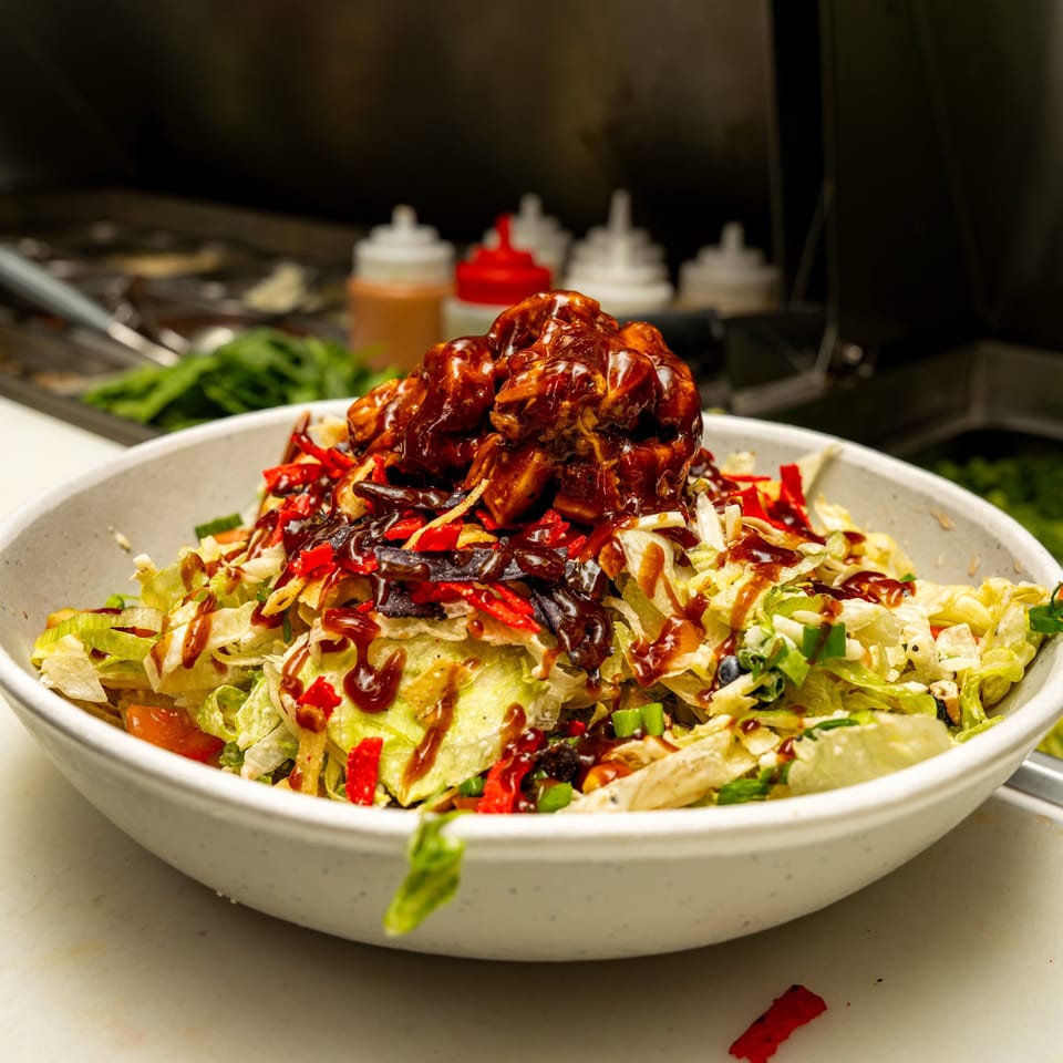Vibrant salad topped with saucy chicken, colorful tortilla strips, and dressing in a white bowl.