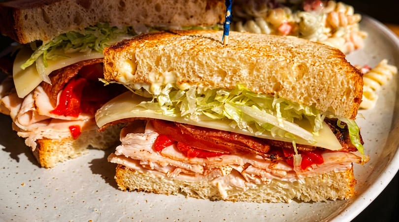 Close-up of a turkey and bacon sandwich with lettuce, cheese, and roasted red peppers.
