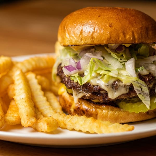 A double cheeseburger with lettuce, onions, and sauce, served with crinkle-cut fries on a white plate.