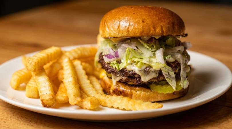 A double cheeseburger with lettuce, onions, and sauce, served with crinkle-cut fries on a white plate.