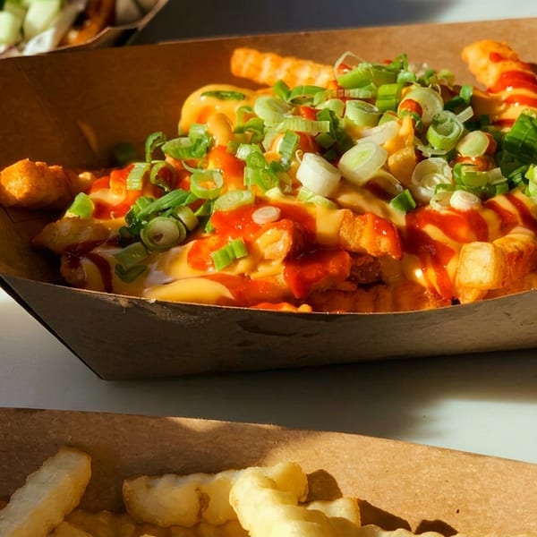 Crispy fries topped with melted cheese, red sauce, and chopped green onions in a paper tray.
