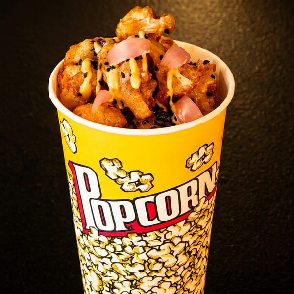 Fried cauliflower bites with sauce, black sesame seeds, and pickled onions in a popcorn cup.
