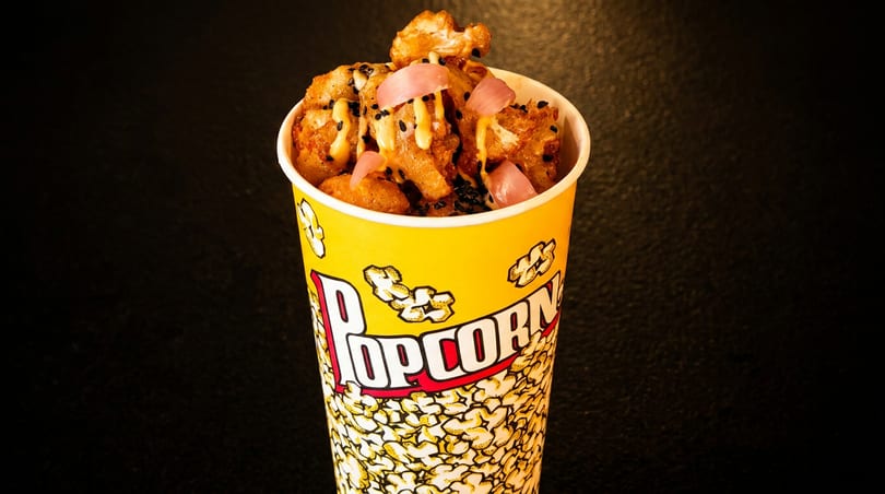 Fried cauliflower bites with sauce, black sesame seeds, and pickled onions in a popcorn cup.