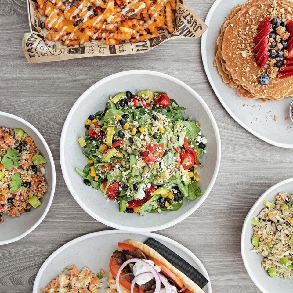 Assortment of restaurant dishes: loaded fries, berry pancakes, fresh salads, and a gyro on a table.